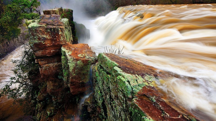 Brown waterfall cascading over mossy rocks