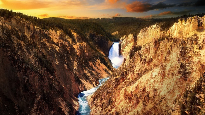 Waterfall in a canyon with pine trees and sunset sky