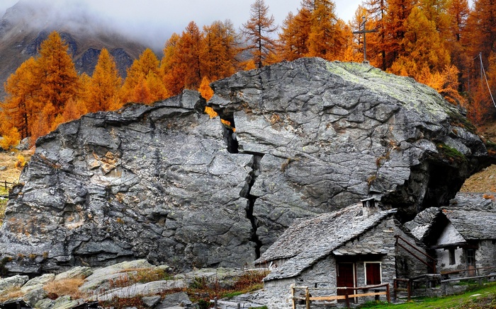 Stone houses and a large boulder in autumn forest
