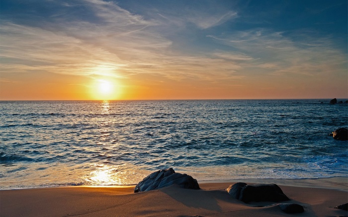 Sunset over the ocean with rocks on the beach