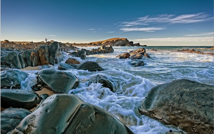 Fisherman on rocky coastline with waves crashing