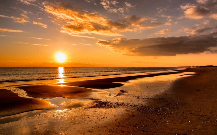 Sunset over a sandy beach with calm ocean waves