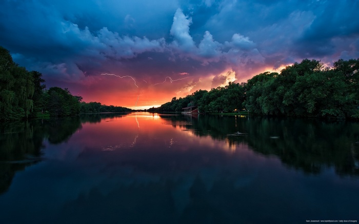 Lightning strikes over a river at sunset