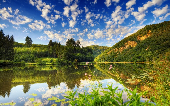 Lake reflecting green hills and blue sky with clouds