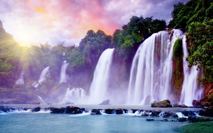 Majestic waterfalls cascade down lush green cliffs under a colorful sky