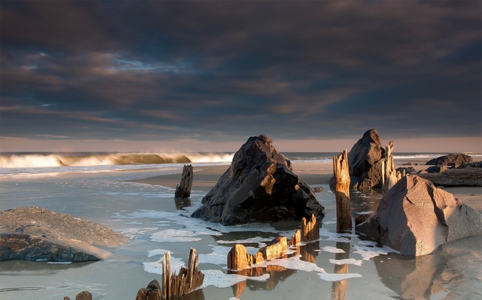 Rocky beach with waves and wooden posts at sunset