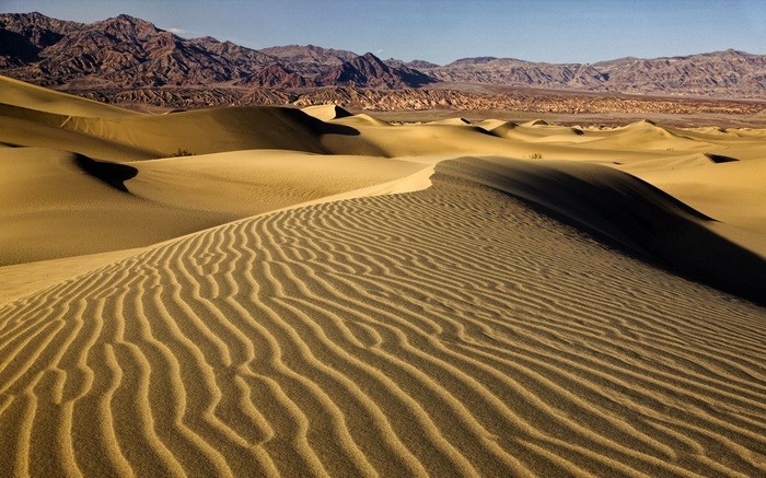 Sand dunes and mountains under a clear sky