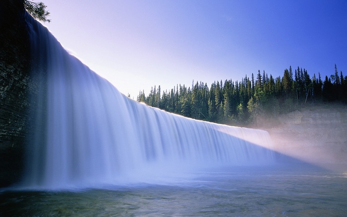 Wide waterfall cascading into a river with a forest backdrop