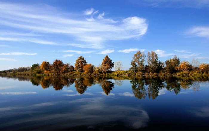 Autumn trees reflected in a calm lake under a blue sky