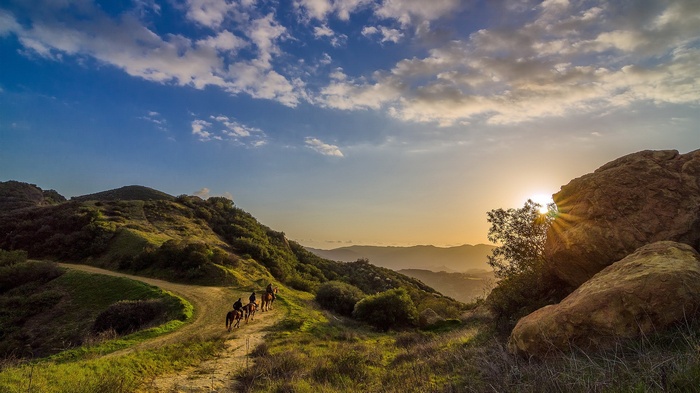 People riding horses on a mountain trail at sunset