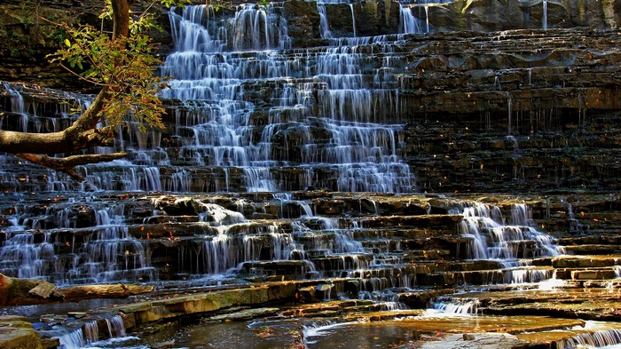 Tiered waterfall cascading over layered rocks with a tree branch