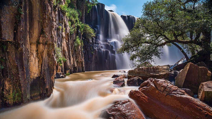 Waterfall cascading over dark rocks with a tree