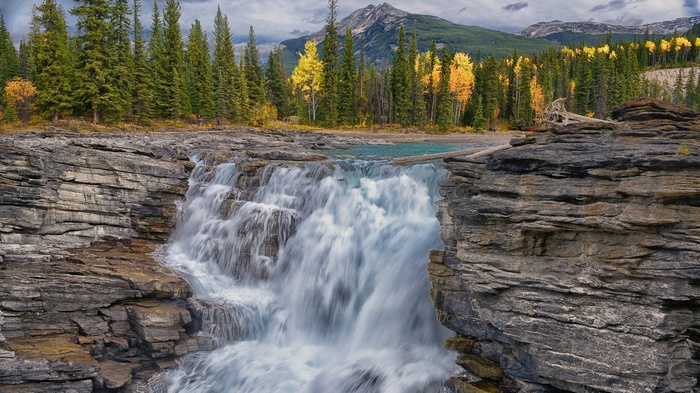 Waterfall cascading over rocks with pine trees and mountains