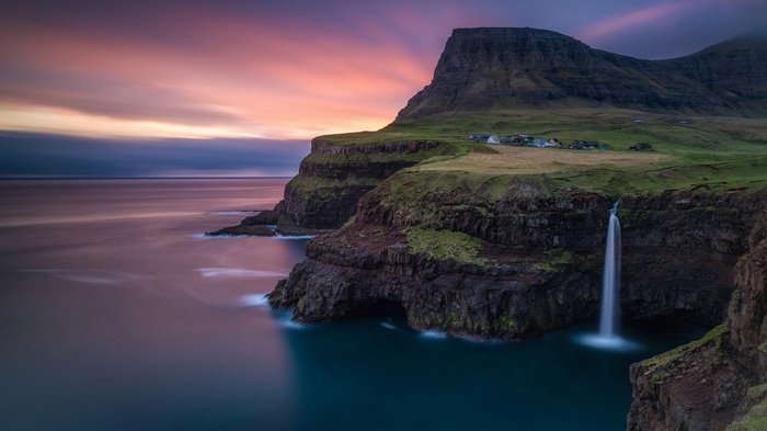 Waterfall cascading from cliffs into the ocean at sunset