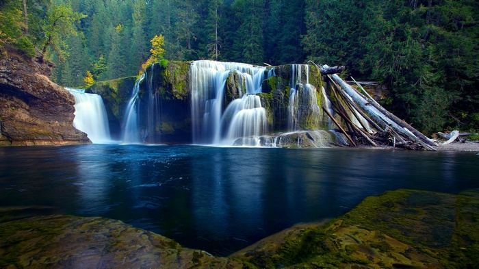 Waterfall cascading into a blue river surrounded by forest