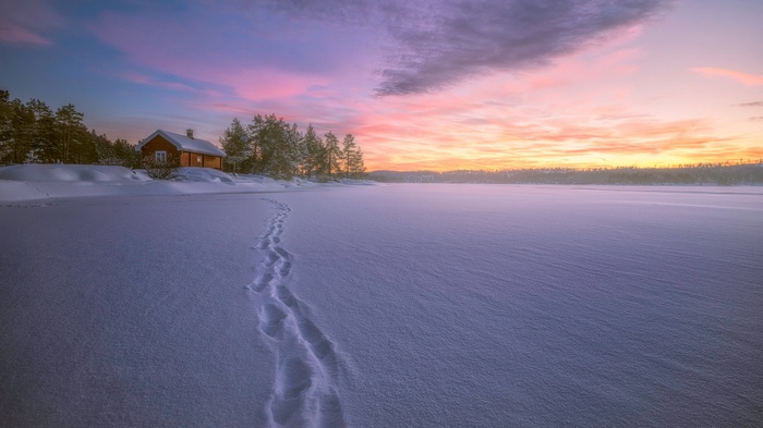 Footprints in snow leading to a cabin at sunset