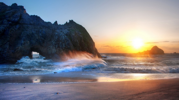 Sunset over ocean with rock arch and waves