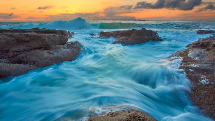 Ocean waves crashing on rocky shore at sunset