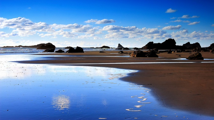 Beach with rocks and reflections under blue sky