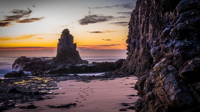 Rocky coastline at sunset with footprints on sand