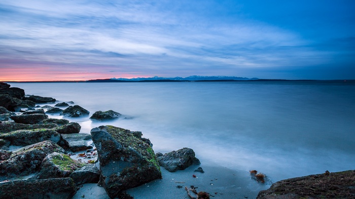 Ocean sunset with rocky shore and distant mountains