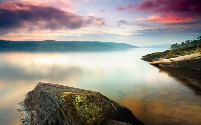 Calm lake at sunset with colorful clouds and rocky shore