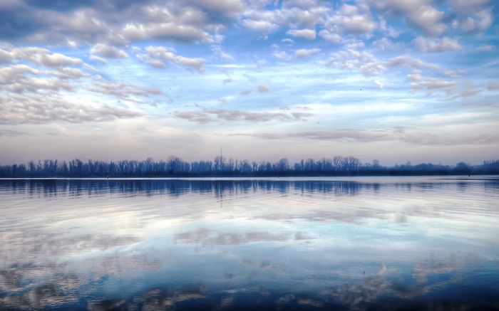 Calm lake reflecting trees and clouds under a blue sky