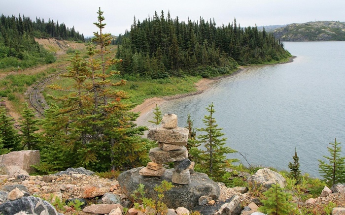 Inukshuk by a lake with train tracks and forest