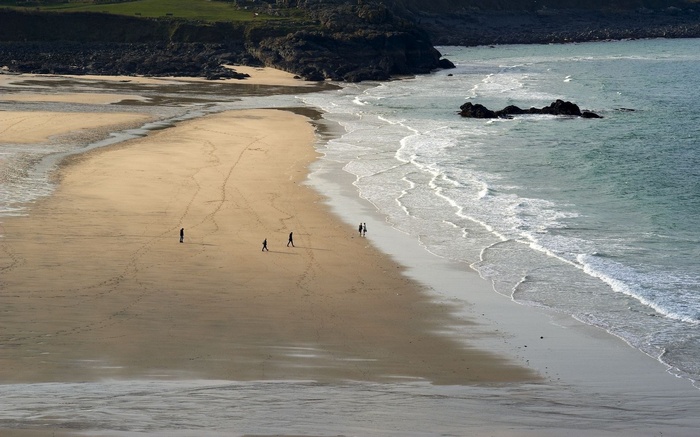 People walking on a sandy beach with waves and rocks