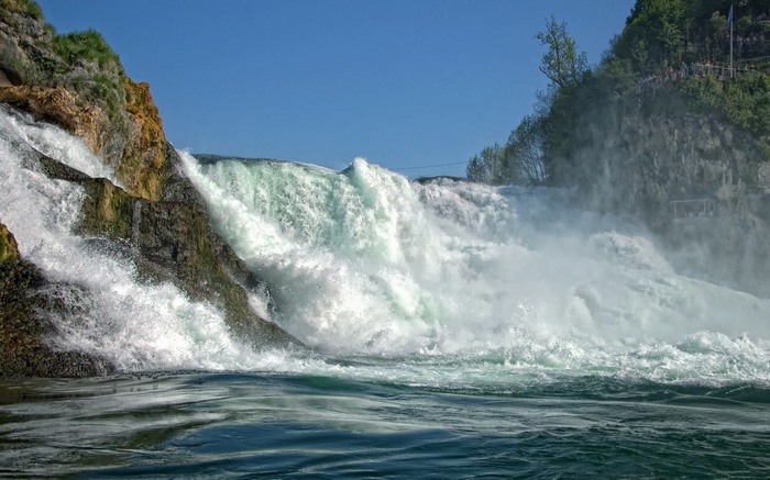Powerful waterfall cascading over rocks under a clear blue sky