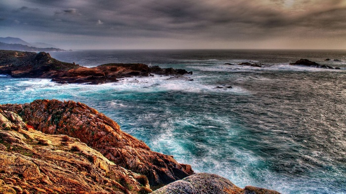 Rocky coastline with crashing waves under a cloudy sky