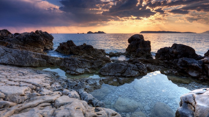 Rocky coastline with calm sea and dramatic sunset sky