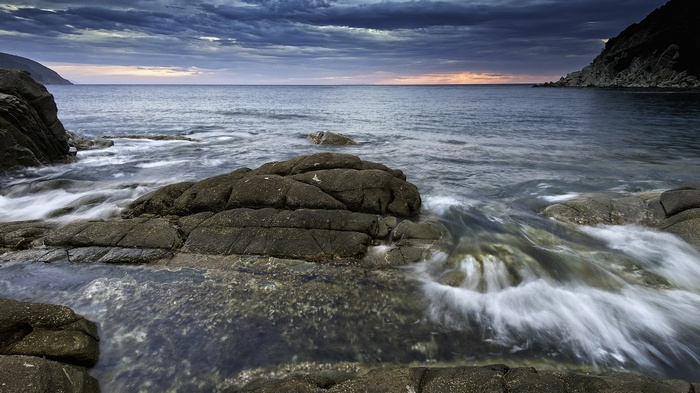 Ocean waves crashing on rocky shore at dusk