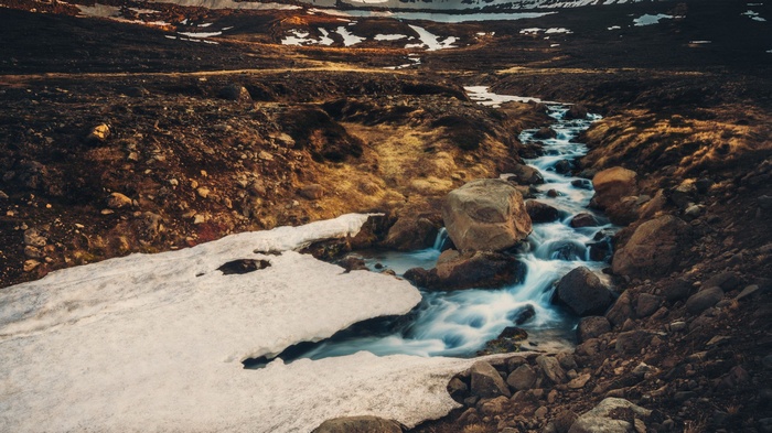 Mountain stream flowing through rocky terrain with snow patches