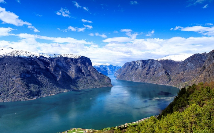 A wide fjord with steep, snow-capped mountains under a blue sky.