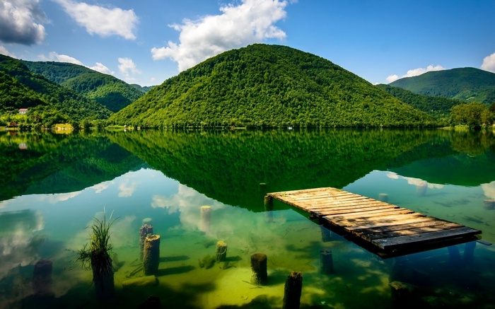 Wooden pier on a clear lake with green mountains