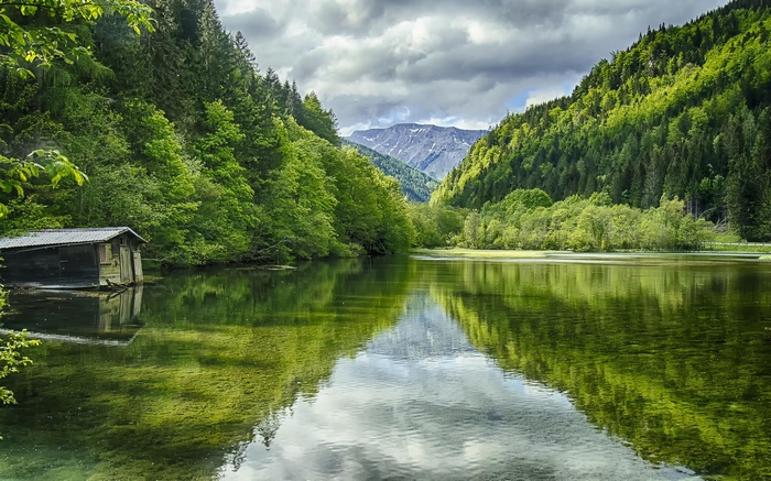 Wooden boathouse on a calm lake surrounded by green forests and mountains