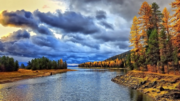 Autumn trees line a lake under stormy clouds
