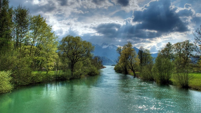 River flowing through trees towards mountains under cloudy sky