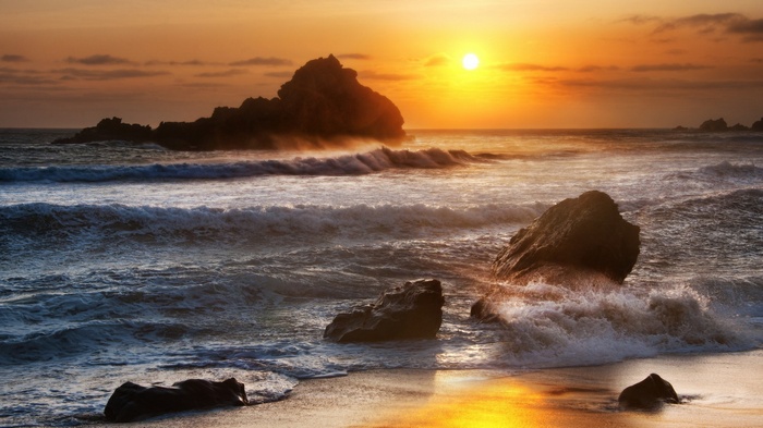 Sunset over the ocean with waves crashing on rocks