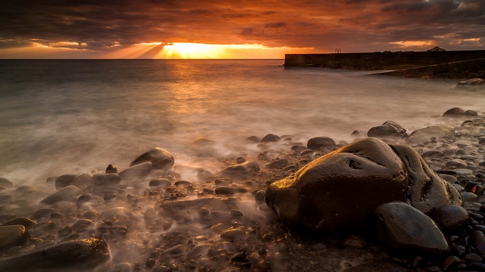 Sunset over rocky beach with pier