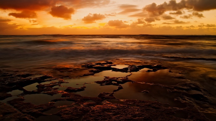 Sunset over the ocean with rocky shore