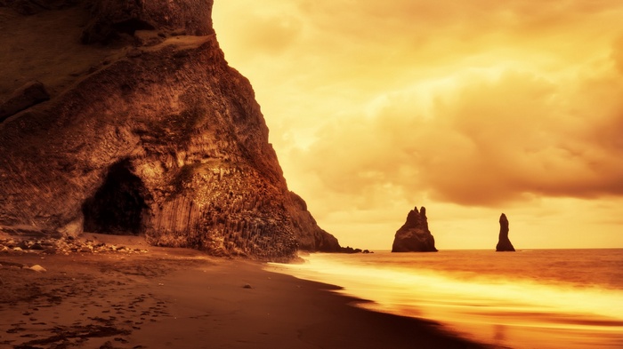 Cave entrance on a black sand beach with sea stacks