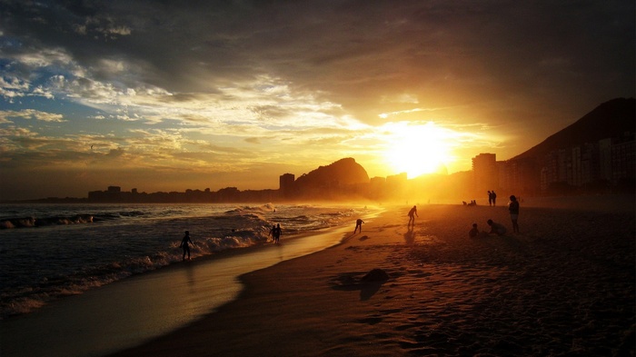 Sunset over a beach with people and city skyline
