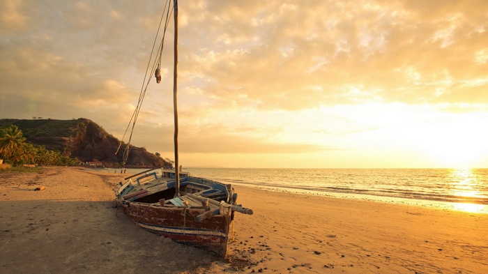 Old wooden boat on a sandy beach at sunset