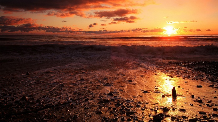 Sunset over the ocean with waves and rocky beach