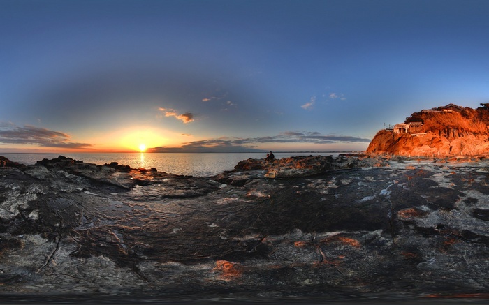 Sunset over rocky coastline with buildings on cliff