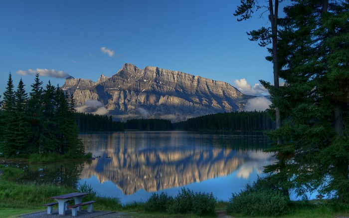 Mountain reflected in a lake with pine trees and picnic table