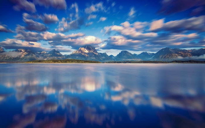 Mountains reflected in a misty lake under a cloudy sky