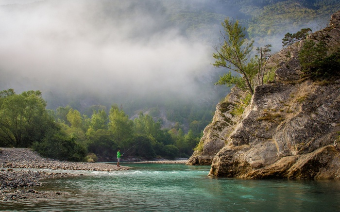 Man fishing in a river with misty mountains